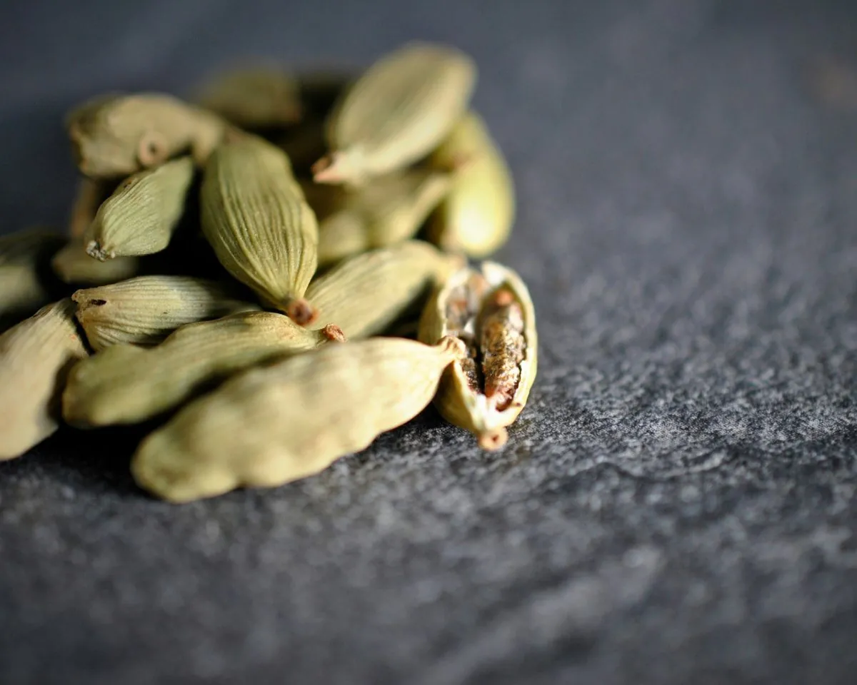 Dried green cardamom pods on dark slate, one split open to show the seeds