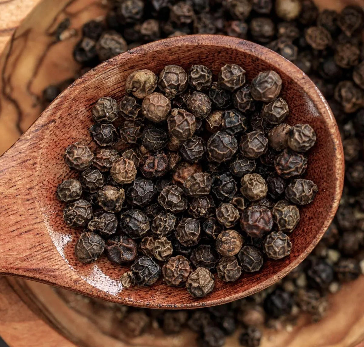 Whole black peppercorns on a wooden spoon