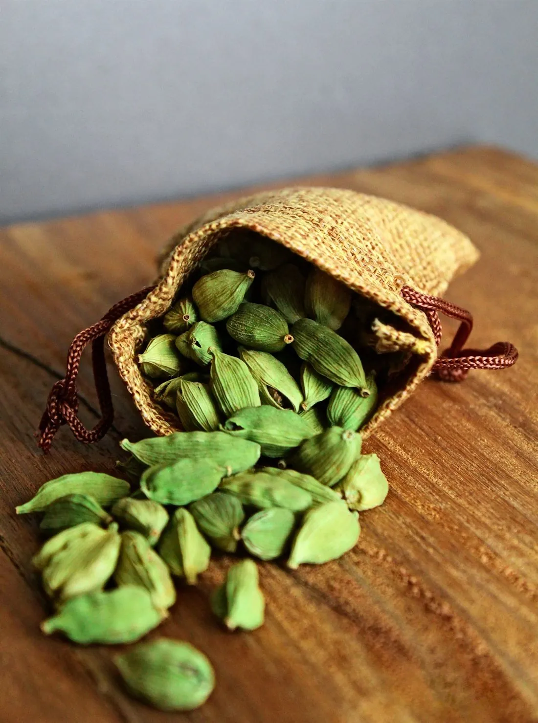 Green cardamom pods spilling from a jute pouch